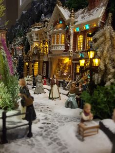 a toy town with people and buildings in the snow at night time, including christmas lights