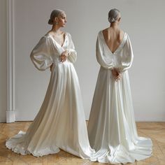 two women in white gowns standing next to each other on the floor with their backs turned