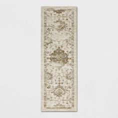 a beige and brown runner rug with an ornate design on the bottom, in front of a white wall