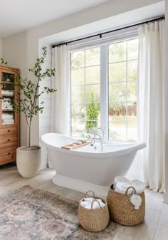 a white bath tub sitting under a window next to a rug and potted plant