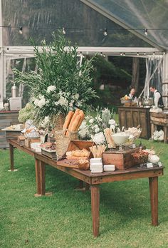 a wooden table topped with lots of food on top of a lush green grass covered field