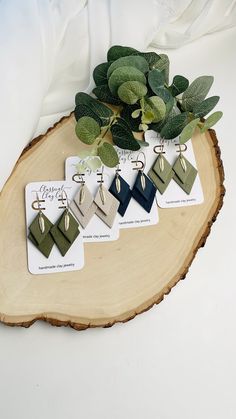 four pairs of earrings are sitting on a piece of wood next to some green leaves