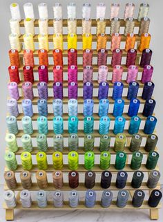 an array of spools of thread on a wooden rack with multiple colors and sizes