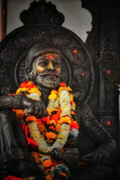 a statue of a man with flowers around his neck sitting in front of a wall