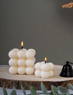 two white candles sitting on top of a wooden table next to a black candle holder