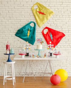 a table topped with cakes and desserts covered in superman capes on top of it