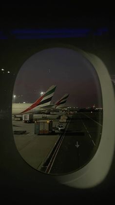 an airplane wing is seen through the window at night, with planes parked on the tarmac in the background