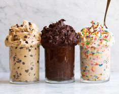 three different types of ice cream in small glass containers with spoons and sprinkles