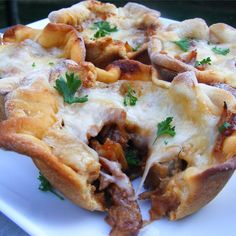 a pizza with meat, cheese and parsley on it sitting on a white plate