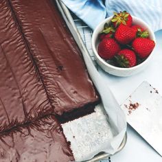 a chocolate cake with strawberries in a bowl next to it on a cooling rack