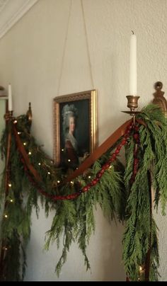 a christmas garland hanging on the wall next to a candle holder with a portrait in it