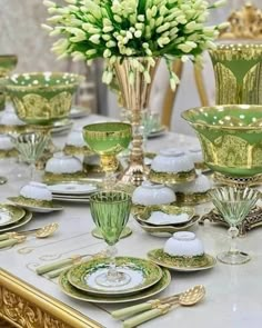 a table topped with lots of green and white dishes next to a vase filled with flowers