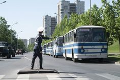 a man standing in the middle of a street with buses behind him and cars driving down the road