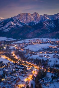 an aerial view of a town in the mountains at night with snow on the ground