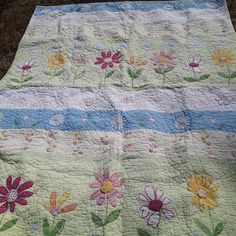 a quilt with flowers on it is laying on the ground in front of some grass