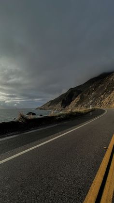 an empty road near the ocean under a cloudy sky