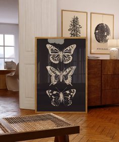 three framed butterflies are on display in a room with wood floors and white walls, along with a wooden coffee table