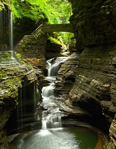 a waterfall with fall leaves on the ground and water cascading down it's sides