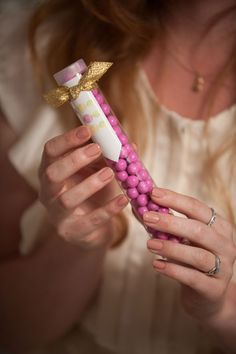 a woman holding a pink and white candy bar with gold bow on it's top