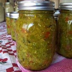 three jars filled with pickles sitting on top of a red and white checkered table cloth