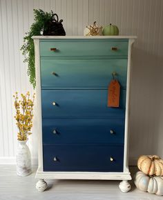 an old dresser painted blue and white with gold knobs on the handles, sitting next to some pumpkins