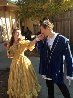 a man and woman dressed up as princesses in front of a house, one holding the other's hand