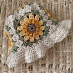 a crocheted dishcloth with a sunflower on it sitting on a wicker surface