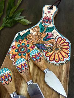 three wooden utensils on a cutting board with flowers and leaves painted on them