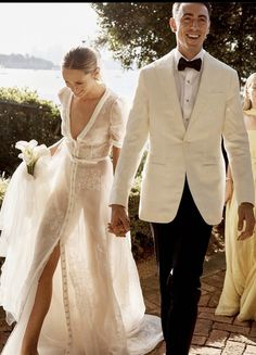 a bride and groom are walking down the path together in their wedding gowns, holding hands with each other