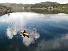 a person in a kayak on the water with mountains in the background and cloudy sky