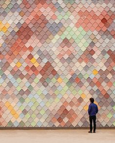 a man standing in front of a wall made of multicolored tiles, looking at the ground