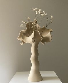 a vase with white flowers in it sitting on a table next to a gray wall