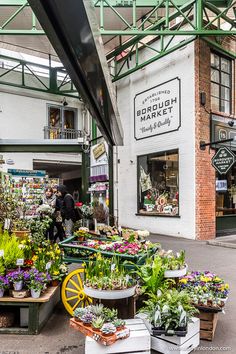 an outdoor market with lots of plants and flowers on the tables in front of it