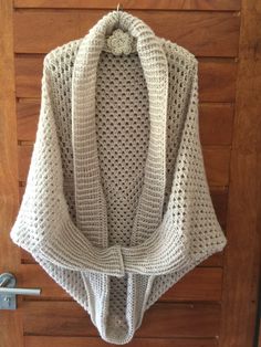 a white crocheted sweater hanging on a wooden door with a hook in it