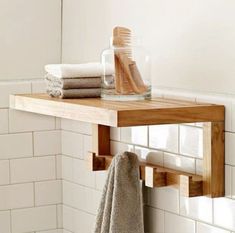 a wooden shelf with towels and toothbrushes on it in a white tiled bathroom