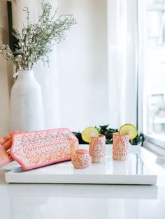 a person holding a tray with three cups and lemons on it next to a vase