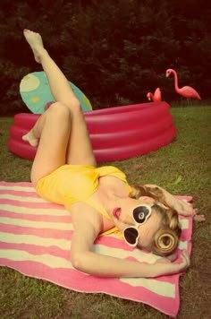 a woman laying on top of a pink and white towel next to an inflatable pool