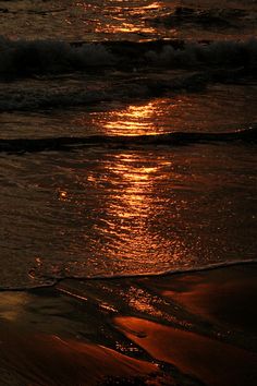 the sun is setting over the ocean with waves coming in to shore and sand on the beach