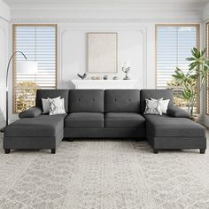 a living room with a large gray sectional couch and pillows on the floor next to windows