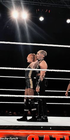 two women in wrestling gear standing next to each other on a stage with lights behind them