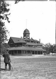 an old black and white photo of a man standing in front of a large building