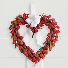 a heart shaped wreath with white bow hanging on the wall