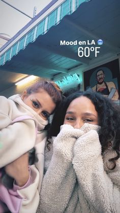 two women are covering their faces while standing in front of a building with an advertisement on it