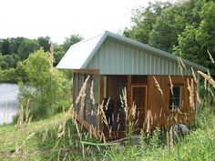 a small cabin sitting on top of a lush green field next to a lake and forest