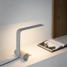 a white table lamp sitting on top of a desk next to an open book and magazine