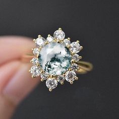 a woman's hand holding an engagement ring with a green and white stone in the center