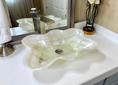 a bathroom sink sitting under a mirror next to a vase with flowers on top of it