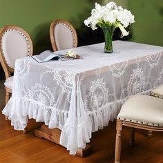 a table with white flowers in a vase on it and two chairs at the end