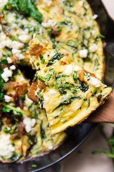 an omelet with spinach and feta cheese is being lifted from a skillet