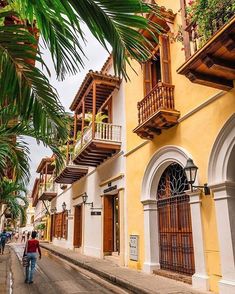 two people walking down the street in front of buildings with balconies and palm trees